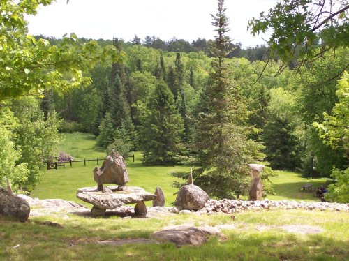 A serene landscape featuring green trees, a grassy area, and large rocks scattered throughout the scene.