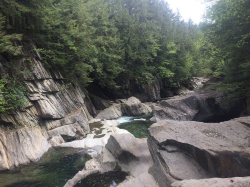 A serene river flows through rocky terrain, surrounded by lush green trees and steep cliffs.