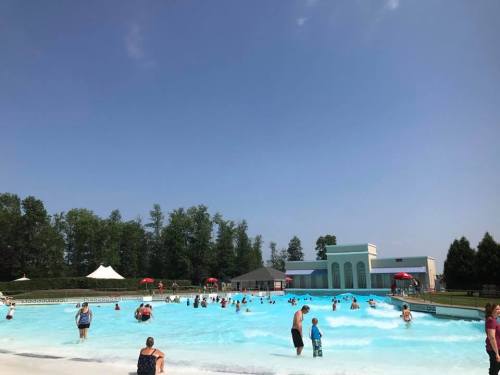 A crowded wave pool on a sunny day, with people enjoying the water and trees in the background.
