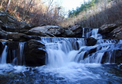 A serene waterfall cascades over rocks, surrounded by trees in a tranquil forest setting.