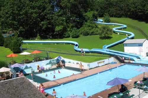 A water park scene featuring a winding slide, a swimming pool, and people enjoying the sun and water activities.