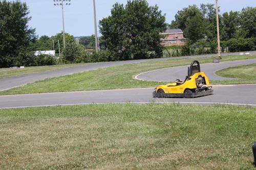 A yellow go-kart speeds around a curved track, surrounded by green grass and trees in the background.