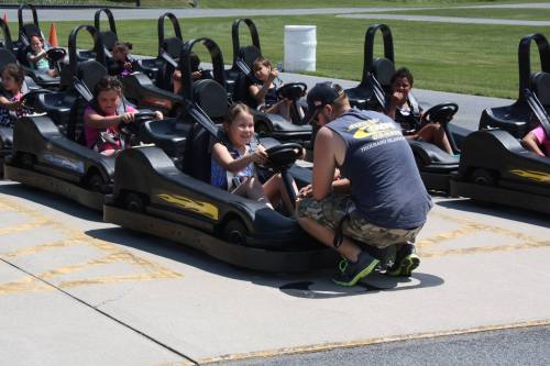 A group of children in go-karts, with one child receiving instructions from an adult on the track.