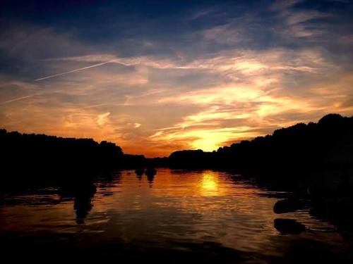 A serene sunset over a calm river, with vibrant orange and purple hues reflecting on the water's surface.