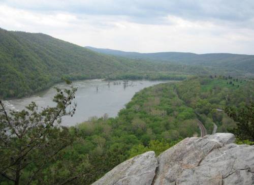 A scenic view of a winding river surrounded by lush green hills under a cloudy sky.