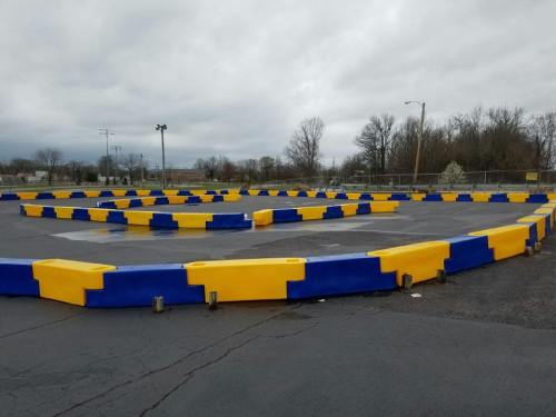 A go-kart track with yellow and blue barriers, set against a cloudy sky and bare trees in the background.