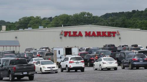 A busy flea market with numerous parked cars in the foreground and a large sign reading "Flea Market" on the building.