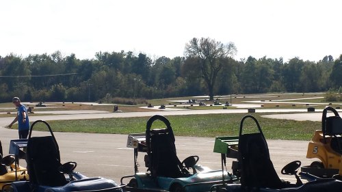 A go-kart track with several parked karts in the foreground and a person walking in the background.