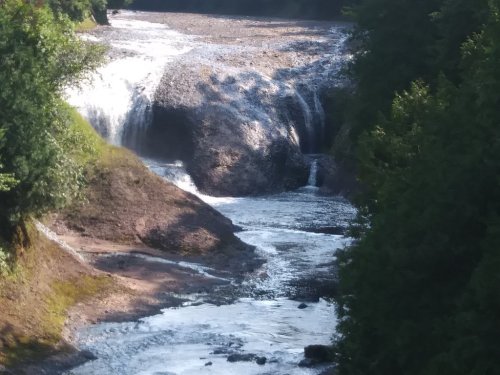 A serene waterfall cascading over rocky terrain into a flowing river, surrounded by lush greenery.