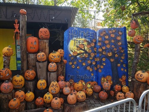 A colorful display of carved pumpkins and a mural titled "Halloween Tree" by Ray Bradbury, set in a festive outdoor area.