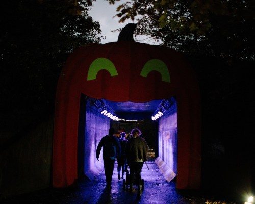 A group of people walks through a large pumpkin-shaped tunnel illuminated by blue lights.