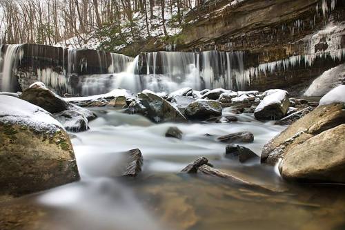 A serene winter scene featuring a waterfall surrounded by icy rocks and snow-covered trees.
