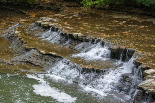 A serene waterfall cascading over rocky ledges into a calm river, surrounded by autumn foliage.