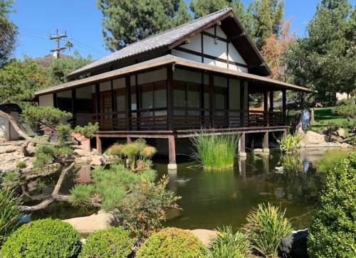 A serene Japanese-style house on stilts surrounded by a pond and lush greenery.