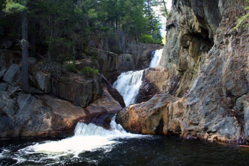 A serene waterfall cascading over rocky cliffs into a calm pool, surrounded by lush green trees.