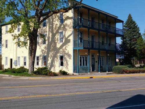 A three-story yellow building with blue balconies, surrounded by greenery and a clear blue sky.