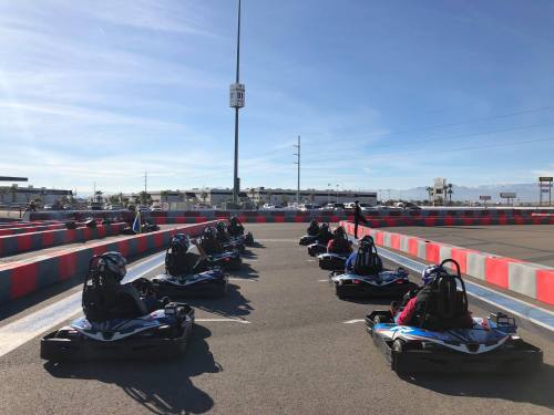 A group of go-karts lined up on a racetrack under a clear blue sky.