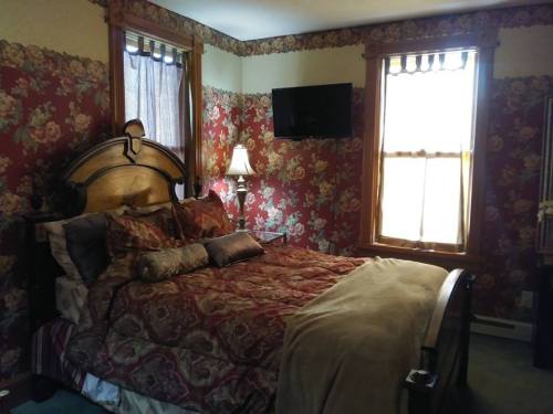 Cozy bedroom with floral wallpaper, a wooden bed, decorative pillows, and a TV mounted on the wall.