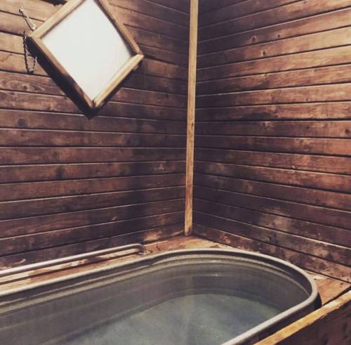 A wooden bathroom with a soaking tub and a framed mirror on the wall. The walls are made of dark wood panels.
