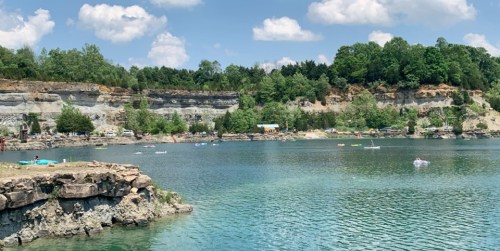 A serene lake surrounded by rocky cliffs and lush greenery, with people kayaking and relaxing on the water.