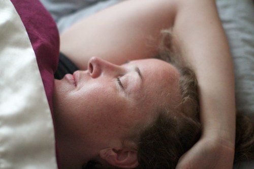 A woman peacefully sleeping with her eyes closed, resting on a bed with a blanket partially covering her.