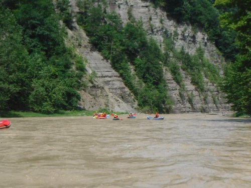 A group of kayakers paddles on a river surrounded by steep, tree-covered cliffs.