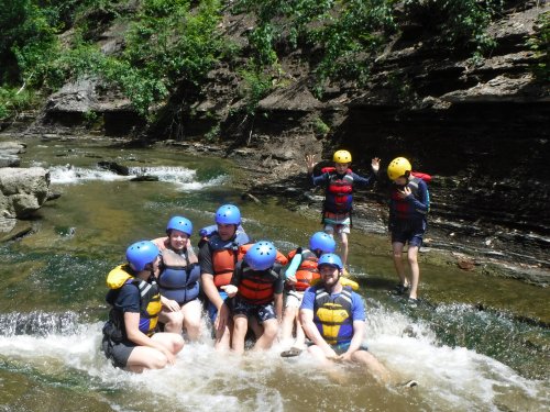 A group of people in helmets and life jackets enjoying a river rafting experience, splashing in the water.
