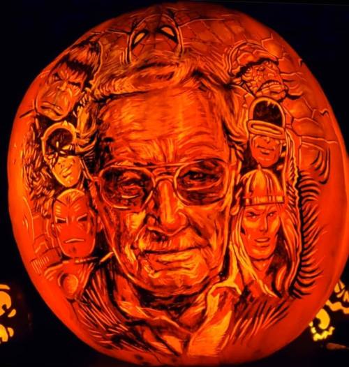 A carved pumpkin featuring a detailed portrait of a man surrounded by superhero faces.