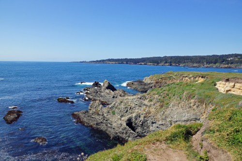 A scenic coastal view featuring rocky cliffs, clear blue water, and a clear sky.