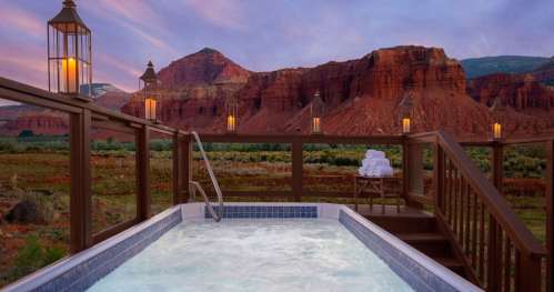 A hot tub on a wooden deck overlooks red rock formations and a scenic landscape at sunset.