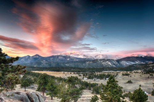 A scenic view of mountains at sunset, with colorful clouds and a lush valley below.