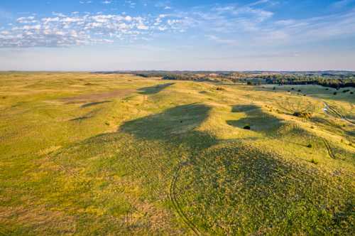 Aerial view of expansive green hills and fields under a clear blue sky with scattered clouds.