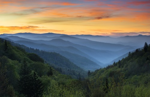 A serene mountain landscape at sunset, with layered hills and a colorful sky.