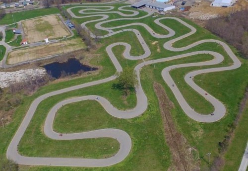 Aerial view of a winding go-kart track surrounded by green fields and a small pond.