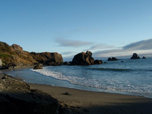 A serene beach scene with gentle waves, rocky formations, and a clear blue sky.