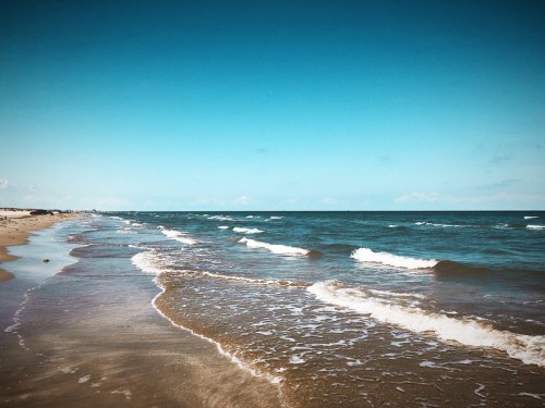 A serene beach scene with gentle waves lapping at the shore under a clear blue sky.