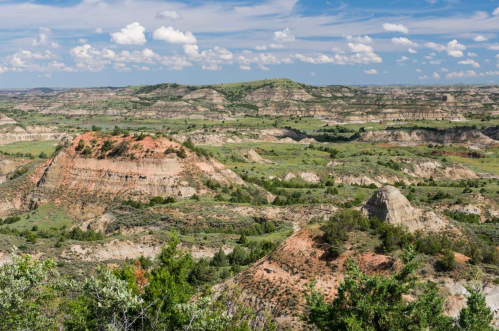 A panoramic view of rolling hills and rugged terrain under a blue sky with scattered clouds.