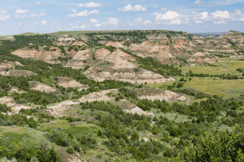 A scenic view of rolling hills and valleys with green vegetation under a blue sky with scattered clouds.