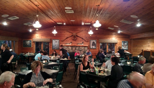 A cozy restaurant interior with wooden decor, tables filled with diners, and staff serving in a warm atmosphere.