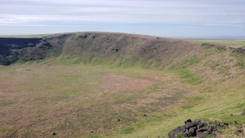 A wide view of a grassy volcanic crater with a gently sloping rim under a clear sky.