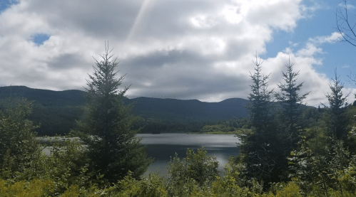 A serene lake surrounded by lush greenery and mountains under a partly cloudy sky.