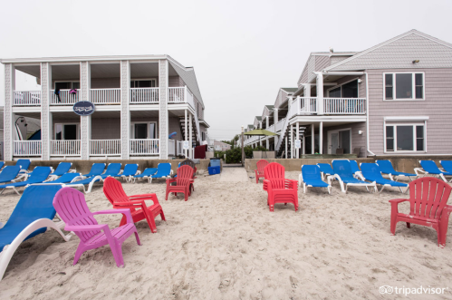 Beachfront view featuring colorful lounge chairs and two multi-story buildings with balconies.