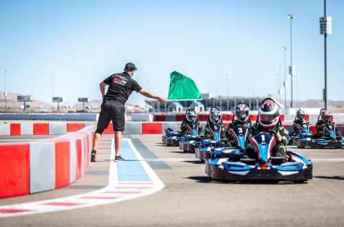 A race official waves a green flag as go-karts line up on a track, ready to start a race.