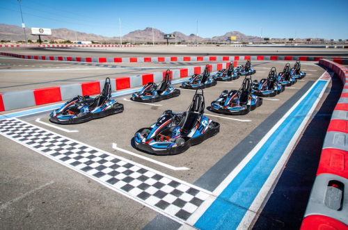A row of go-karts lined up at a racetrack, with a checkered finish line in the foreground and mountains in the background.