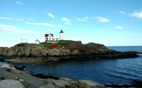 A scenic lighthouse on a rocky shore, surrounded by water and a clear blue sky.
