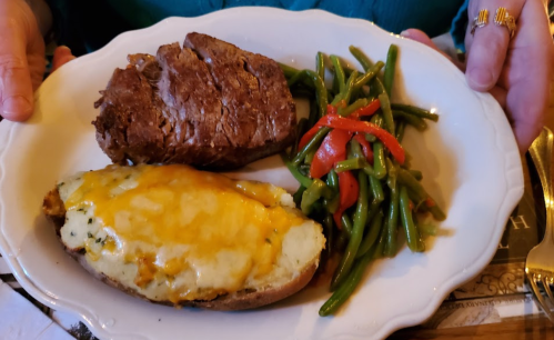 A plate with a baked potato topped with cheese, green beans, red peppers, and a slice of meatloaf.