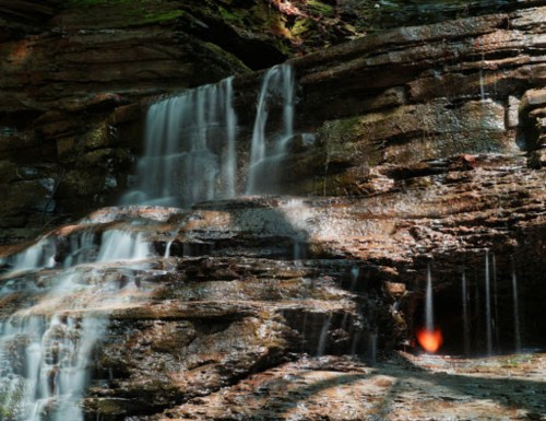 A serene waterfall cascading over rocky cliffs, with sunlight filtering through the trees, creating a tranquil atmosphere.
