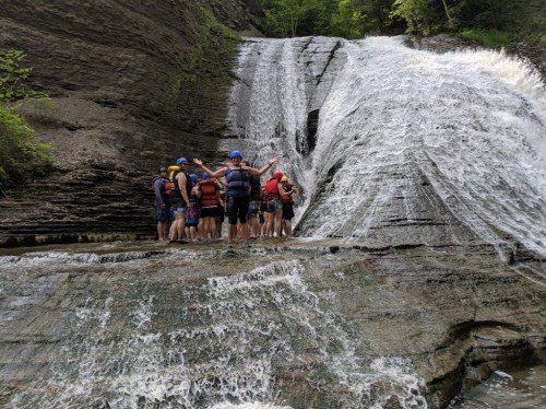 A group of people stands at the base of a waterfall, enjoying the natural scenery and water splashing around them.
