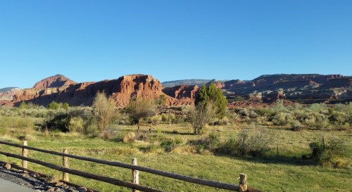 A scenic view of red rock formations and green fields under a clear blue sky.