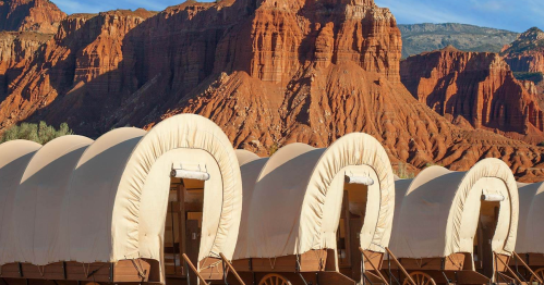 Covered wagons lined up against a backdrop of red rock formations and blue sky.